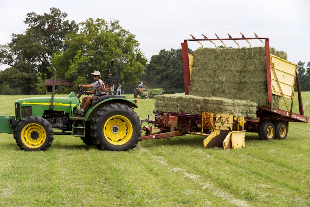 A farmer operating a green tractor loading hay in a rural North Carolina field.