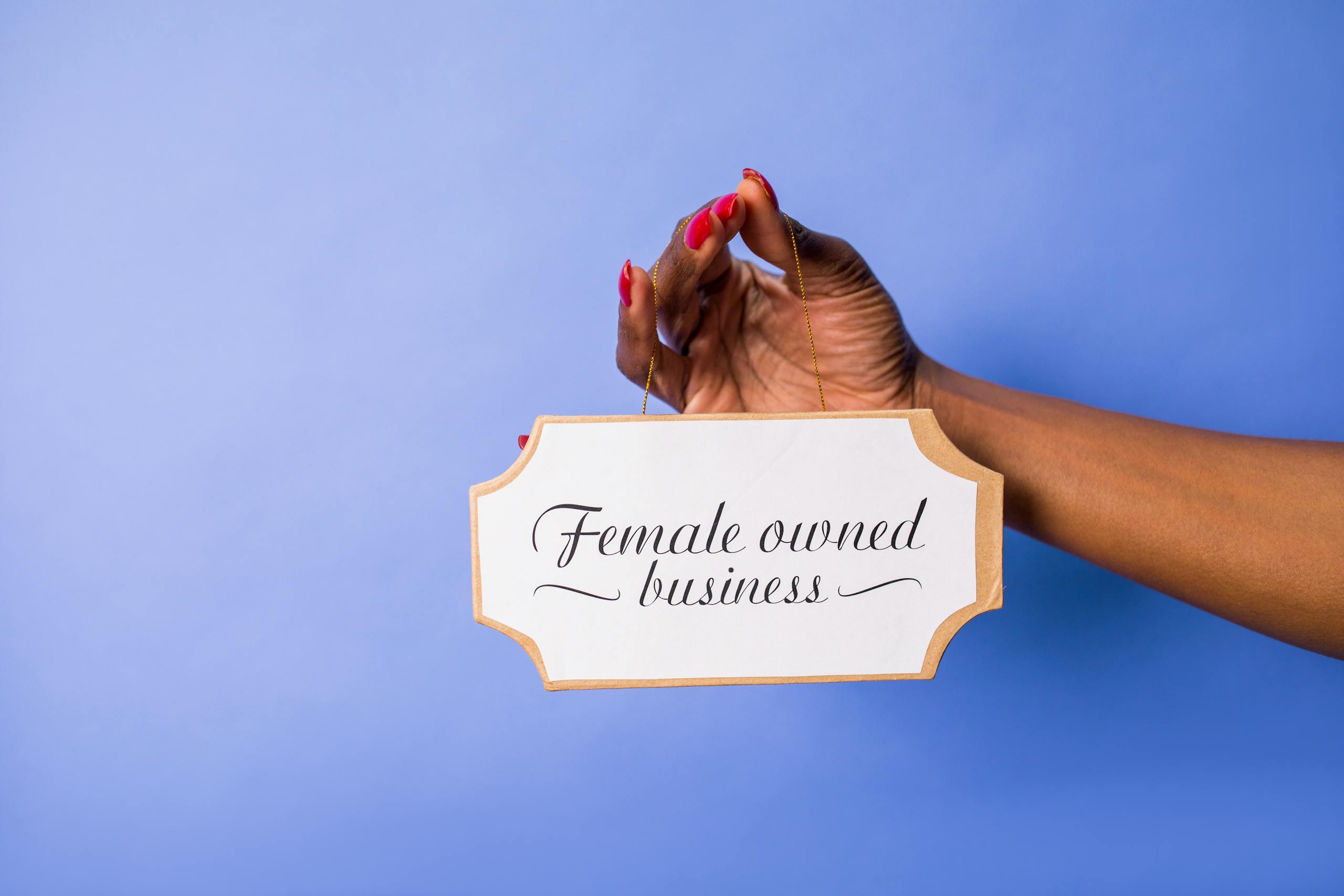 A hand holding a 'Female owned business' sign against a blue background, signifying empowerment.