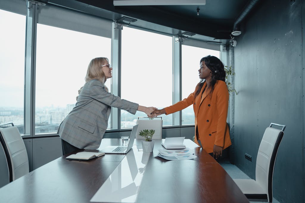 Two businesswomen shaking hands in a modern office setting, symbolizing partnership and agreement.